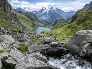 Hiker at the mountain stream and mountain lake Lac de Louvie with glaciated summit of the Grand