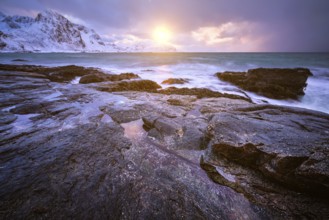 Beach of Norwegian sea on rocky coast in fjord on sunset in winter. Vareid beach, Lofoten islands,
