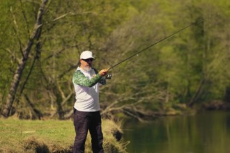 Man fish with spinning on river bank, casting lure. Outdoor weekend activity. Photo with shallow