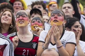 Women wearing make-up in the German national colours watch the football match in the fan zone at