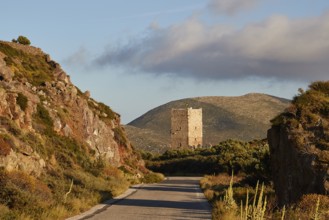A road leads to an old tower in a mountainous landscape during the golden hour, residential tower,