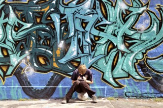 Ten-year-old boy playing with his Nintendo in front of a graffiti wall, football pitch, Germany,