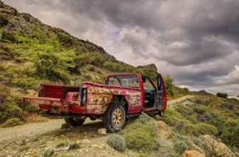 An old, rusty pickup truck in mountainous nature under a cloudy sky, wrecked vehicle, Crete, Greek