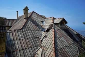 Dilapidated roofs of an old building with red tiles and a chimney under a clear blue sky, Mussolini