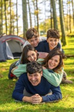 Vertical photo of a caucasian cheerful family laughing while lying down together at forest next to
