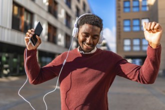 Happy african man listening to music with mobile and headphones dancing in the city street