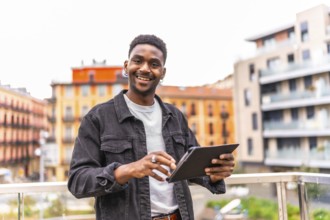 African young man smiling at camera while using digital tablet in the city