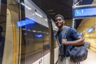 African young businessman waiting for the metro at night standing on the platform and smiling at