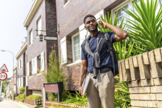 African young man talking to the mobile carrying laptop in the street