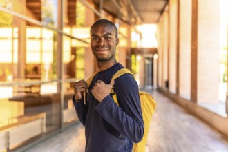 Happy african american student standing with rucksack smiling at camera at the corridor of the