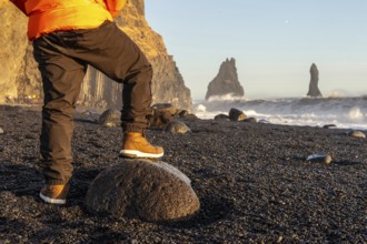 A person is standing on a rock on a beach. The beach is rocky and the sky is blue