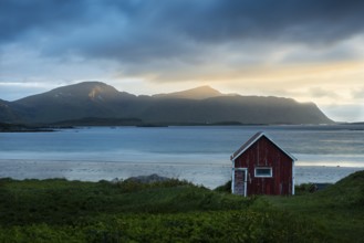 A red wooden hut on the sandy beach of Ramberg (Rambergstranda), with the sea behind it. At night