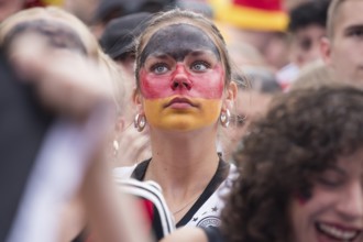 A woman wearing make-up in the German national colours watches the football match in the fan zone