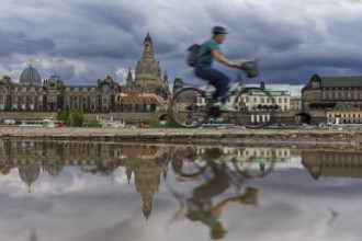The Dresden silhouette with a cyclist and dark clouds behind the Church of Our Lady is reflected in