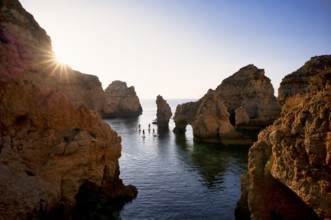 Stand up paddlers on their boards, kayakers, colourful cliffs and sunrise, rocks in the sea, Ponta