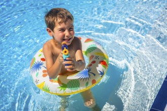 Boy playing with water gun and rubber ring inside the pool