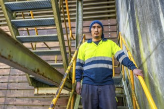 Latin male worker of a recycling plant standing in outside stairs looking at camera with proud look