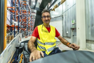 Portrait of a happy mature male worker driving forklift at distribution warehouse