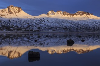 Snow-covered mountains reflected in a fjord in the evening light, Berufjördur, East Fjords,