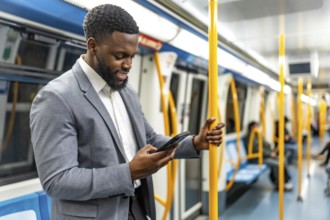 Smiling businessman holding a pole while using a smartphone, standing inside a subway train during