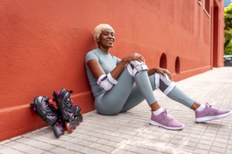 Beautiful african woman roller skating resting sitting on ground and leaning on red facade during