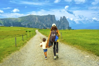 Mother and son walking on a gravel road at alpe di siusi, enjoying summer vacation in the dolomites