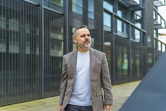 A mature businessman with jacket and casual clothes walking outside block office in the city