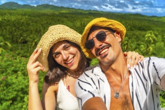 Young couple smiling and taking a selfie with a tropical forest in the background during their