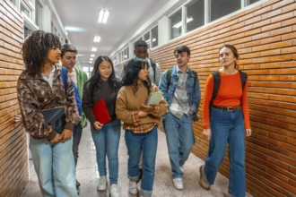 Multi ethnic university students walking down school hallway, chatting and holding books and