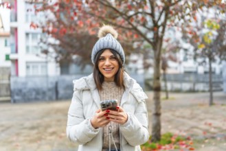 Happy caucasian young woman in warm clothes using phone in the city in winter