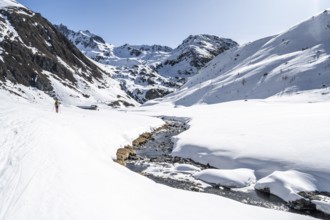 Ski tourer in the snow by a mountain stream in the Funtauna Valley, Graubünden Haute Route, Albula