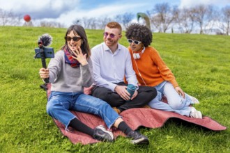 Three friends are recording a video blog in a park, using a smartphone with external microphone
