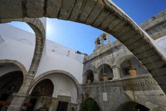 Historic monastery courtyard with stone arches, a tower and hanging plants. Impressive