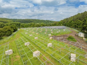 Solar panels on a green area under a cloudy sky in the middle of a wooded landscape, construction