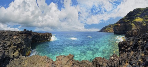 Panoramic view of a rocky lava coast with clear blue water and clouds in the sky, Termas da