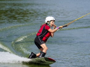 Boy or girl with wakeboard in lake, eating bread, water sports, water skiing in wakepark