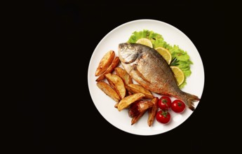 Fried Dorado fish, with potatoes, top view, on a black background, no people