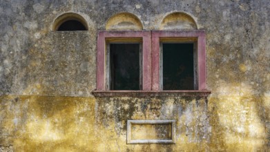Two old windows in a dilapidated, yellow façade with heavily faded and peeling areas, Italian