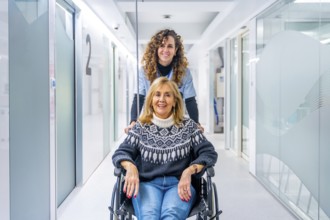 Happy nurse carrying mature female patient in wheelchair at the hospital corridor