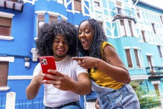 African friends pointing to a mobile with surprised expression standing next to blue colorful