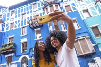 African american cool couple taking selfie with mobile in a street with colorful facades