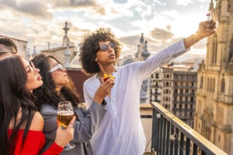 Young man taking selfie with two beauty women in rooftop party with city views during sunset