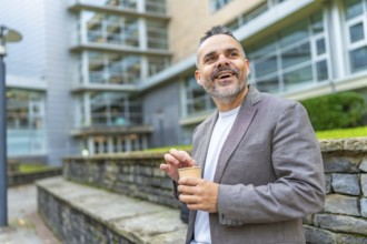 Happy mature caucasian businessman enjoying coffee break outside the block office in the city