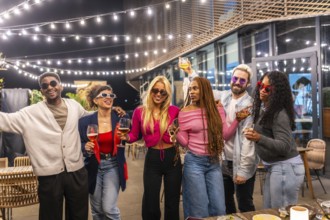 Group of young diverse multi-ethnic friends having fun at bar terrace decorated by lights at night