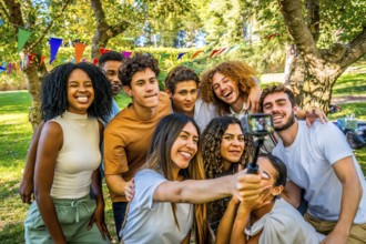Smiling multi-ethnic friends taking selfie with wearable camera at park while celebrating birthday