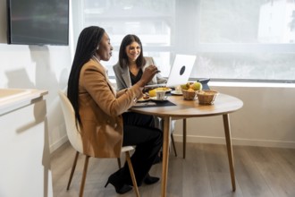 Two businesswomen having breakfast and working on a laptop in their hotel room during a business