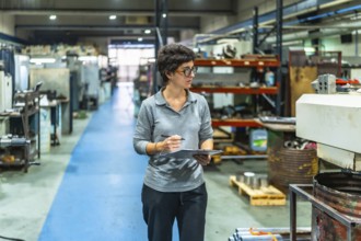 Female caucasian manager of a metallurgic cnc factory doing inventory holding a clipboard walking