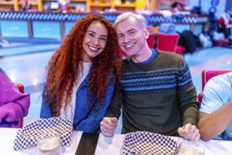 Young multiethnic friends enjoying a meal together at a bowling alley restaurant, celebrating their
