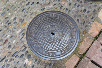 Manhole cover installed in Alquezar in 1966, surrounded by uneven paving stones, manhole cover,