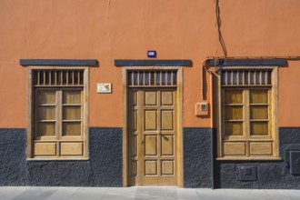 A building facade with an orange wall, wooden door, and windows. The base is painted black,